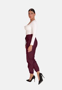Witte langslobige top met een ronde hals, gecombineerd met bordeaux joggingsbroek met elastische tailleband en enkelsokken, en zwarte hoge hakken.