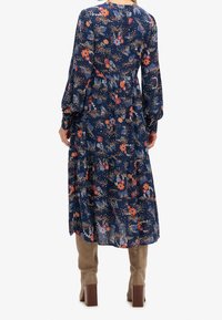 Abito floreale navy con maniche lunghe, design a strati e vita cinchata. Presenta motivi floreali colorati e una texture leggera e fluida.
