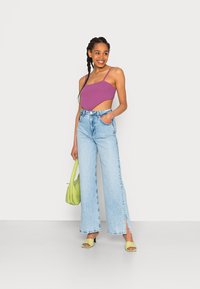 Top curto tricotado roxo com alças finas, jeans de perna larga azul claro com fendas na barra, mala verde e sandálias de salto bloco amarelas.