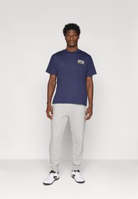 T-shirt de algodão azul-marinho com o texto "JUVENTUS MILLES37" no peito, combinado com calças de moletom cinza claro e sapatilhas brancas de desporto.