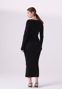 Čierne rebrované midi šaty s dlhými rukávmi a výstrihom do oblúka, ktoré zvýrazňujú priliehavú siluetu a hladkú textúru. Doplnok tvorí strieborné lodičky.