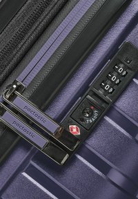 Valigia viola con superficie testurizzata, doppie cerniere e una combinazione di blocco con il logo TSA. I tiranti delle cerniere sono brandizzati "pactastic".