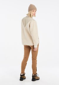 Beige fleece pullover met een tan paneel, relaxte pasvorm en geribbelde manchetten. Gecombineerd met bruine slim-fit broek en donkere wandelschoenen.