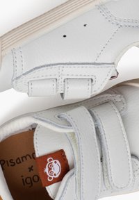 Weiße Ledersneaker mit Klettverschlüssen, runder Spitze, strukturiertem Obermaterial und einem braunen Etikett mit einem Cartoon-Bear im Inneren des Schuhts.