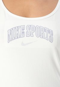 Hvit ermeløs topp med teksten "NIKE SPORTS" i lilla søm og en liten grå Nike swoosh-logo under teksten.
