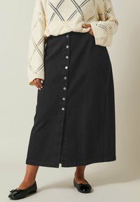 Gonna midi in denim nero con chiusura a bottoni frontale, caratterizzata da una silhouette dritta e tasche laterali, abbinata a un maglione a maglia color crema.