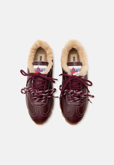 Paire de baskets en cuir rouge foncé avec des coutures blanches épaisses, une doublure beige duveteuse, des lacets à motifs et des étiquettes de marque sur la languette.