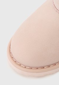 Light pink suede ankle boot with a rounded toe, featuring a smooth texture and contrasting tan stitching along the outsole.