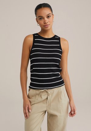 Black and white striped sleeveless top with a textured knit design. The bottom hem is fitted, and the model pairs it with beige drawstring trousers.