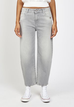 Hellgraue Jeans mit weitem Bein, getragen von einer Person mit weißen High-Top-Sneakern und einem weißen, kurzen Pullover, stehend vor einem schlichten Hintergrund.