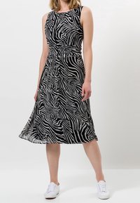 Robe midi rayée noir et blanc avec une taille ajustée, sans manches et une jupe fluide. Stylée avec des baskets blanches.