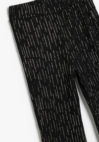 Leggings negros con una tela texturizada y rayas plateadas verticales. La cinturilla es elástica y el diseño general es ajustado.
