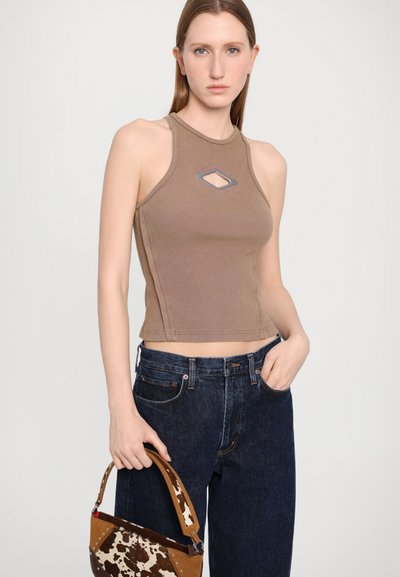 Braunes, geripptes Tanktop mit einem diamantförmigen Ausschnitt, kombiniert mit dunkelblauen Jeans. Das Model hält eine braun-weiße Handtasche mit Muster.