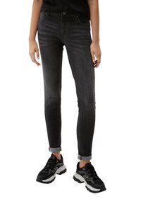 Jeans negros ajustados con un ligero desgaste, diseño de cinco bolsillos y puños enrollados, combinados con zapatillas negras y grises.