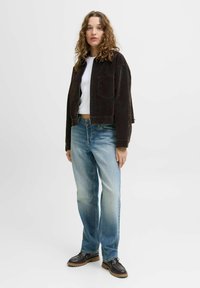 Bruine corduroy cropped jas, witte t-shirt, vervagende blauwe rechte jeans en donkere laarzen met gestructureerde zolen. Eenvoudige, casual outfit.