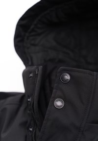 Schwarze Jacke mit hochstehendem Kragen, verstellbarem Kapuzen, Reißverschluss und metallischen Druckknöpfen. Glattes Material mit sichtbaren Nähdetails.