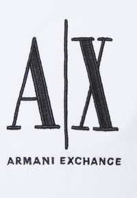 Tessuto bianco con testo ricamato nero: logo "A/X" sopra "ARMANI EXCHANGE". Presenta un carattere audace e moderno e un design pulito.