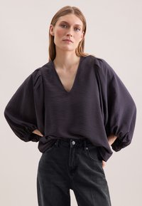 Mørkeblå top med dyb V-udskæring, struktureret stof og ballonærmer. Sættet er kombineret med sorte højtaljede jeans.