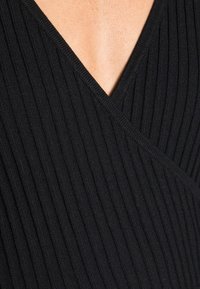 Svart ribbad stickad topp med V-ringning och textilstruktur, som betonar vertikala linjer för en åtsittande silhuett.