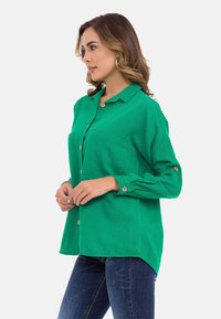 Groen button-up shirt gemaakt van lichte stof, met een kraag, twee borstzakken en opgerolde mouwen, gecombineerd met donkere jeans.