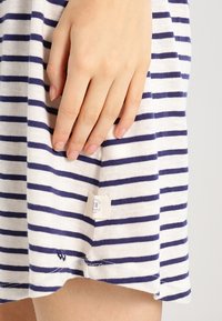 Main dans un tissu de robe rayé bleu marine et blanc avec une petite étiquette blanche près de l'ourlet.