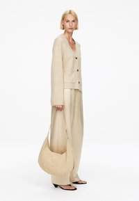 Beige Strickjacke mit V-Ausschnitt und Knöpfen vorne, kombiniert mit cremefarbenen weit geschnittenen Hosen und einer weichen, lässigen beigen Tasche.