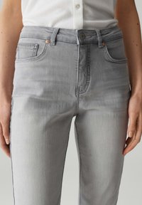Jeans en denim gris au design ajusté, cinq poches, quincaillerie de ton cuivré et légère décoloration sur la texture du tissu.
