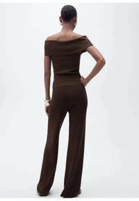 Ensemble en tricot marron composé d'un haut décolleté et d'un pantalon à jambes larges. Texture lisse avec un corsage ajusté et une silhouette fluide.