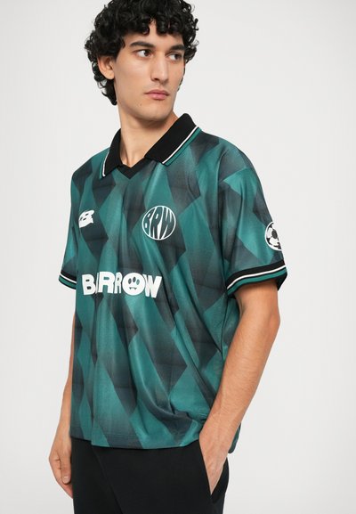 Grün und schwarz gemusterte kurzärmelige Fußballtrikots mit einem Kragen, ausgestattet mit einem Logo und weißem Text. Glattes Gewebe mit geometrischem Design.
