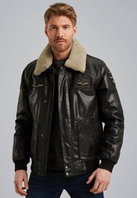 Chaqueta bomber de cuero negro con cuello de borrego, parches en la parte delantera y puños de canalé. Cuenta con cierre de cremallera y bolsillos laterales.