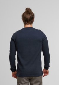 Camicia a maniche lunghe blu navy con scollatura rotonda e texture a coste, con taglio dritto e orlo leggermente curvo sul retro.