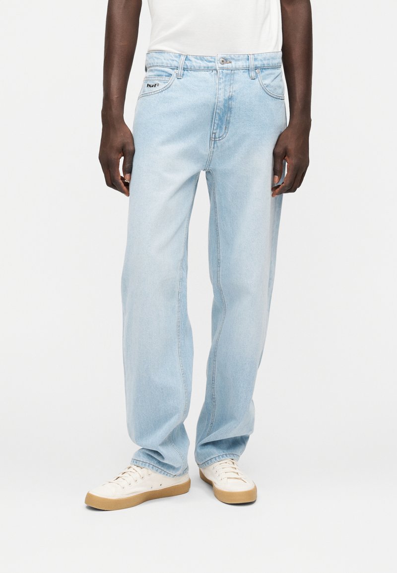 Φωτεινό γαλάζιο τζιν με άνετη εφαρμογή, ανθεκτικό ύφασμα ντένιμ, μπροστινές τσέπες και κεντημένο λογότυπο στη μέση. Φορεμένο με κρεμ παπούτσια.