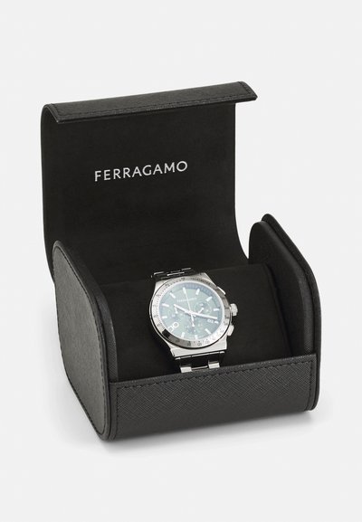 Strieborné chronografické hodinky Ferragamo s kovovým remienkom vystavené v otvorenom čiernom puzdre s logom Ferragamo na bielom pozadí.