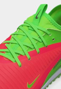 Κοντινό πλάνο αθλητικού παπουτσιού Nike σε νέον πράσινο και φωτεινό κόκκινο χρώμα, με πράσινα κορδόνια και μικρό μαύρο λογότυπο Nike στη γλώσσα και στην πλευρά.