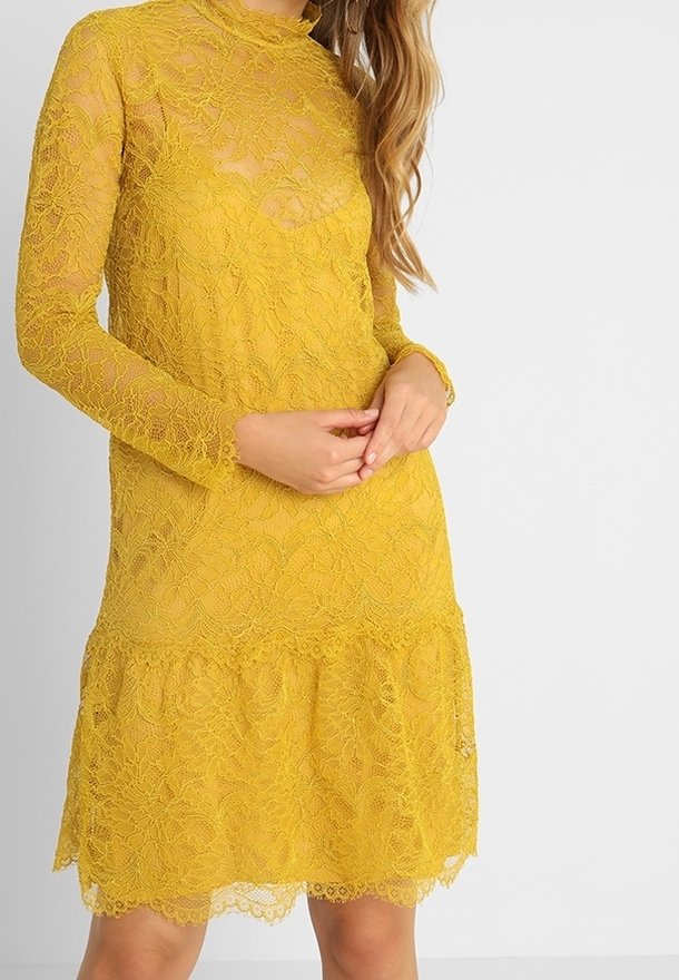 Robe en dentelle jaune texturée avec manches longues, col haut et ourlet à volants. Tissu transparent révélant un design à plusieurs couches.