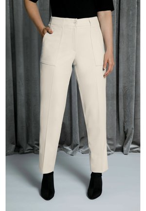 Pantaloni beige chiaro con una vestibilità su misura, dotati di due tasche frontali e una texture liscia. Abbinati a stivali neri alla caviglia.