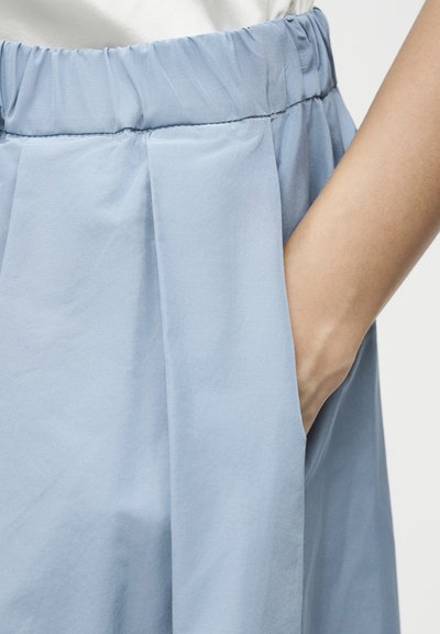 Χέρι στην τσέπη ανοιχτό μπλε, ψηλόμεσου παντελονιού με ελαστική μέση, φορεμένο με λευκό τοπ.