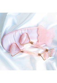 Ensemble de rouleaux de visage en quartz rose sur une surface satinée, comprenant un masseur en forme de papillon, des accents dorés et des têtes de rouleau texturées.