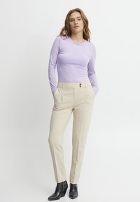 Maglia a maniche lunghe di colore viola chiaro abbinata a pantaloni beige su misura con due pieghe frontali e due bottoni rotondi in vita. Stivaletti neri alla caviglia.