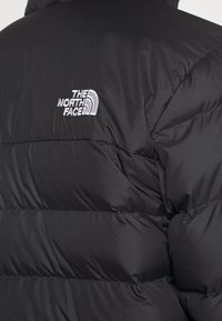 Black puffer jacket with horizontal quilting, featuring white embroidered "The North Face" logo on upper left back.