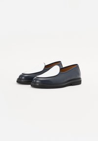 Navy blue leather slip-on shoes with a distinctive white curved panel on the toe, textured upper, and black rubber sole.