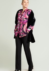 En pink og lilla mønstret silkeskjorte med en sort imiteret pelsindpakning, kombineret med sorte bukser og højhælede sko.