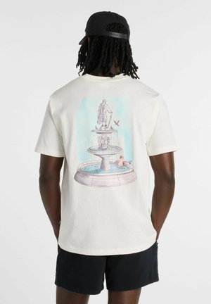 Person wearing black cap, white t-shirt with fountain and statue graphic, and black shorts, viewed from the back against a plain background.