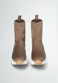 Stivaletti alla caviglia in suede marrone con un design attillato, suola bianca e dettaglio del logo sul lato. Texture morbida e stile minimalista.