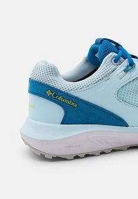 Zapatilla deportiva de color azul claro con materiales de malla y ante, con acentos en azul oscuro, una suela acolchada y el logotipo "Columbia" en el lateral.
