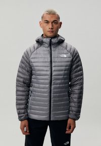 Jacheta gri insulated, cu fermoar frontal, design matlasat și glugă. Dispune de un logo alb pe pieptul stâng și manșete elastice.
