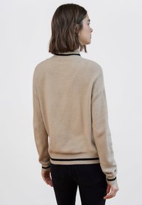 Maglione beige lavorato a maglia con collo a costine e righe nere sui polsini e sull'orlo. Tessuto morbido, vestibilità rilassata e maniche lunghe.