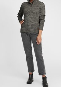 Pull en maille grise avec un col haut et trois boutons marron, associé à un jean gris et des bottines noires. Le tissu texturé ajoute de la profondeur.