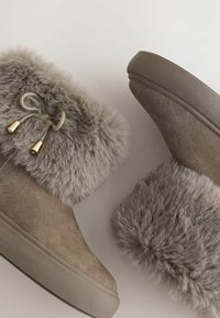 Grijze suède enkellaarsjes hebben een fluffy nepvacht manchet met een decoratieve strik en goudkleurige hardware. De zool is textuur voor grip.