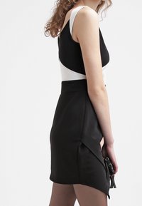 Czarna i biała dopasowana sukienka z okrągłym dekoltem, z asymetrycznym fasonem, gładką teksturą i bokami z elementami ze sprzętem.